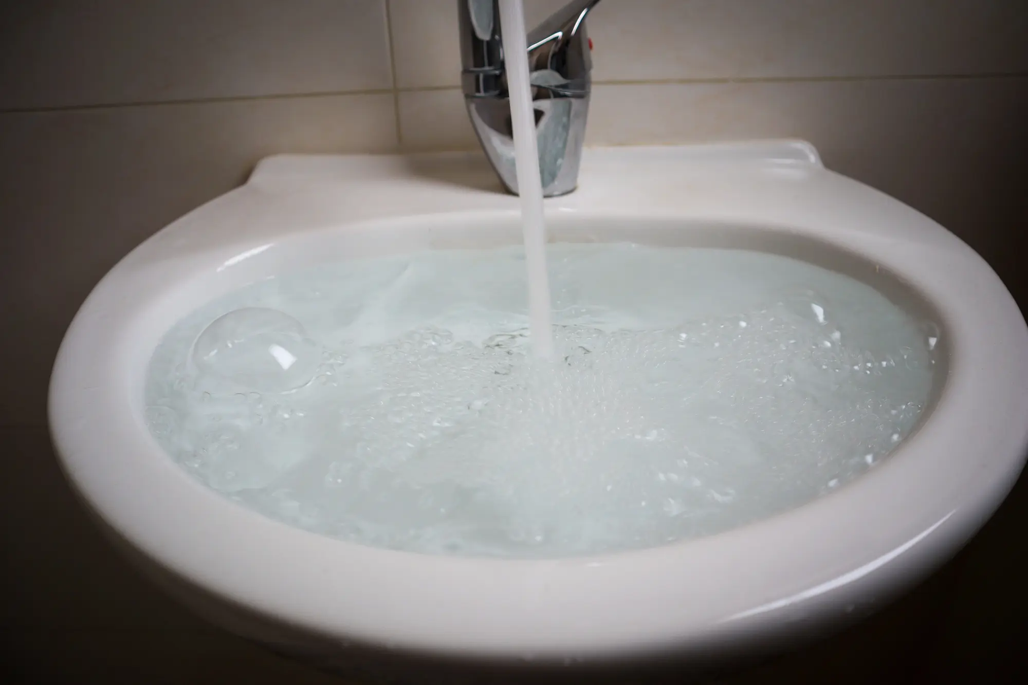 Clean running water flowing from kitchen faucet into white sink basin